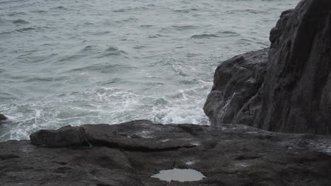 grey moody day while ocean waves hitting rocky coastline, static view