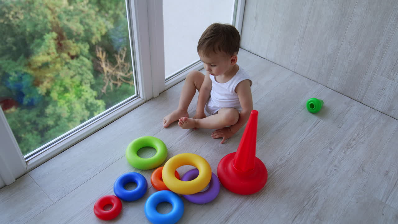 Little kid learning colors with the help of a game. Adorable baby plays with toy pyramid sitting in the balcony. Top view.