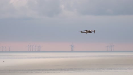 drone se cierne sobre el agua con un parque eólico en segundo plano.