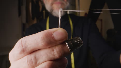 close-up of a tailor's hands threading a needle with a thimble