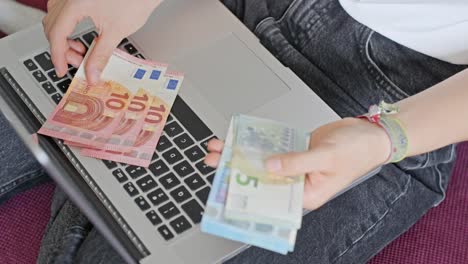 hands of young woman counting euros on laptop, view from above