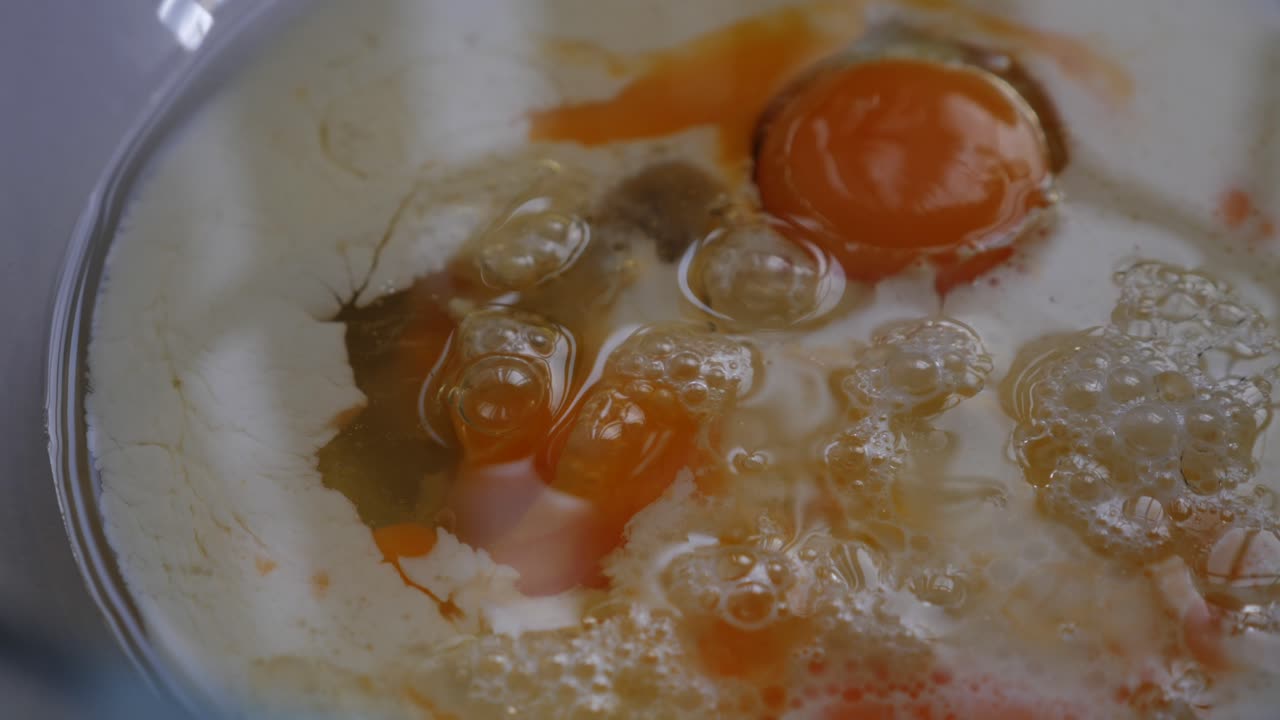 Slow motion pan around baking ingredients of egg, milk and oil in glass bowl with low depth of field