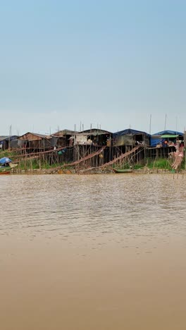 Vertical boat view of stilt houses along Cambodia's riverbank of Chong Khneas under a clear day.