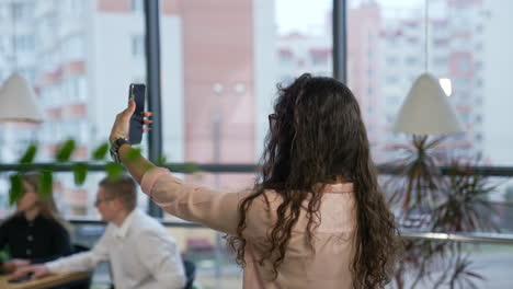 attractive young woman takes selfie in office. female employee shooting video on her mobile phone while turning around.