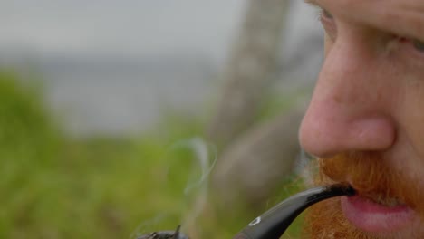 a close up shot of a bearded ginger man lighting a tobacco pipe