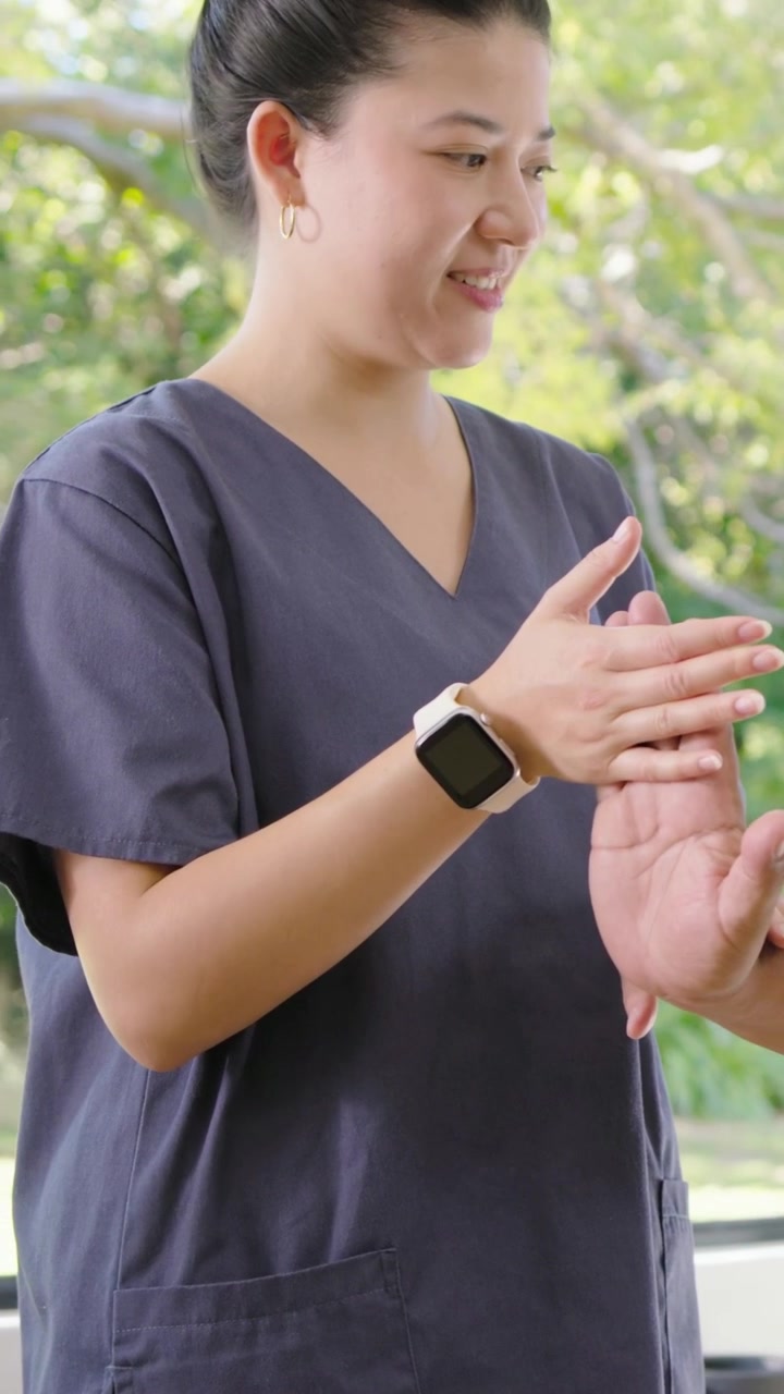 Video verticale: Cliente che offre la mano mentre il terapista in camice preme il polso alla finestra per la riabilitazione.