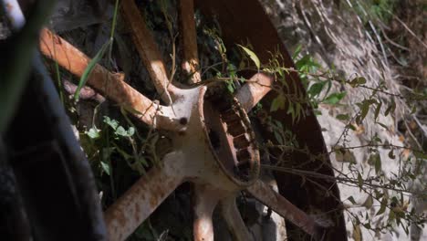 Vieja-Rueda-De-Metal-Oxidado-De-La-Agricultura-Contra-Un-Muro-De-Piedra-Con-Zarzas-En-El-Campo-De-Francia-Verano-Sensación-De-Calma