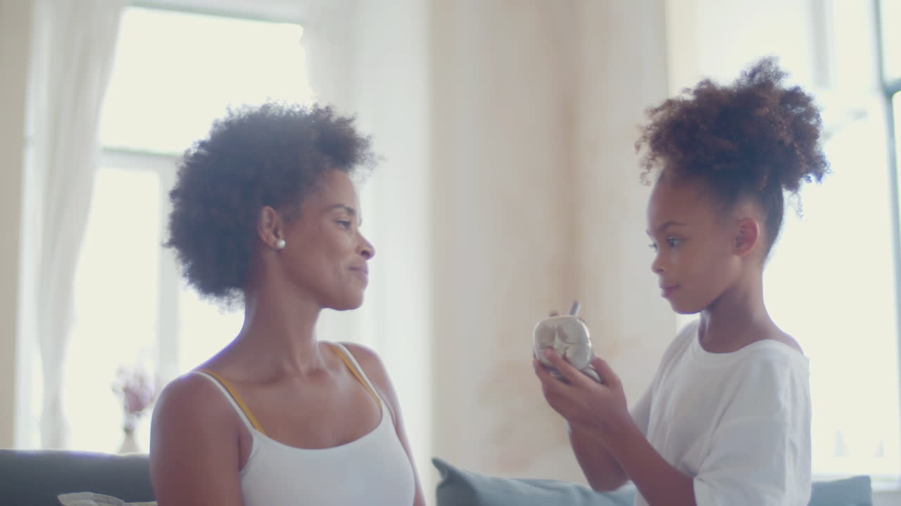 Cute Black girl doing make-up on her mother
