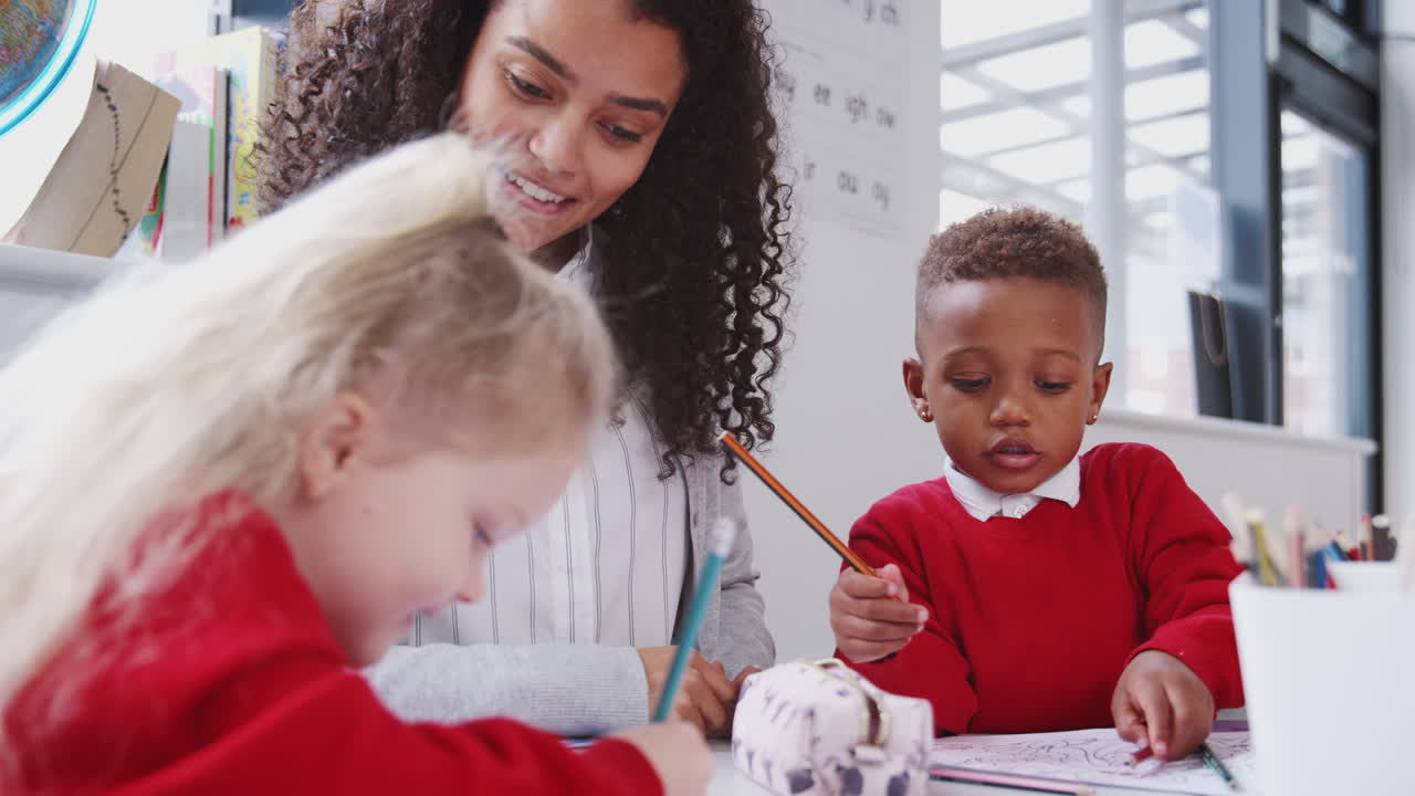 una maestra de escuela infantil sonriente sentada en una mesa con niños dibujando, enfoque selectivo