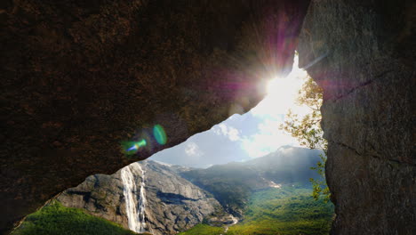 The-Sun-Shines-Through-A-Hole-In-The-Rock-Where-You-Can-See-Mountains-With-A-Waterfall-And-A-Picture