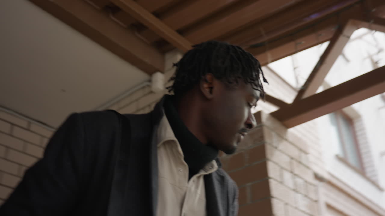 Head level shot tracks footballer in long suit with laptop bag shifting aside from pillar, stepping out toward exit, composed stride, business travel vibe, intentional move revealing structure detail