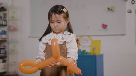 little girl playing with a long balloon in the shape of a dog in classroom in a montessori school