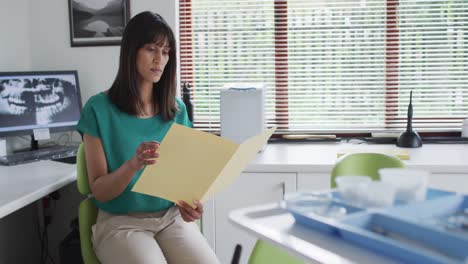 portrait of smiling biracial female patient holding documents at modern dental clinic