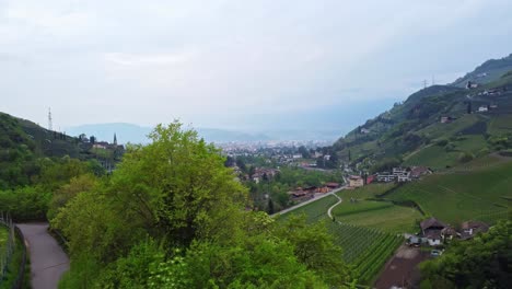 drone slowly ascends above the green slopes near castel roncolo, unveiling winding roads, vineyards, and the renon basin nestled in the alpine region of trentino-alto adige in val sarentino