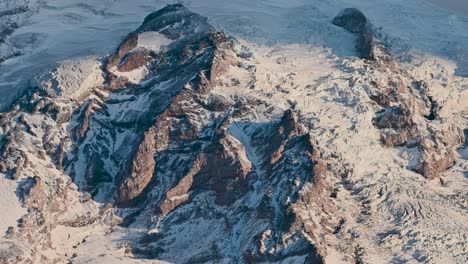 aerial drone view of rugged snow-covered mountain peaks casting long shadows in golden hour light mount rainier