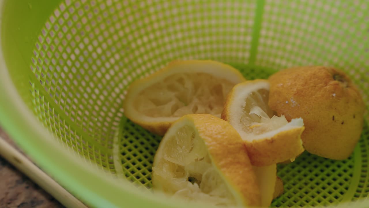 juiced lemon halves in a green plastic colander on a kitchen counter with soft daylight