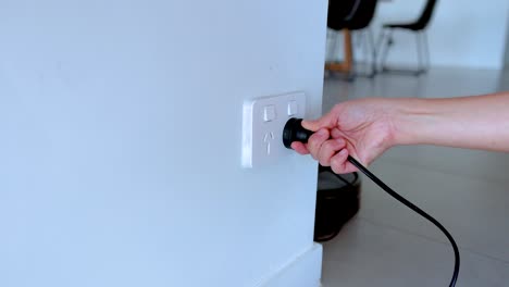 A hand plugs a power cord into a wall socket in a bright, modern room. The sequence captures the action smoothly