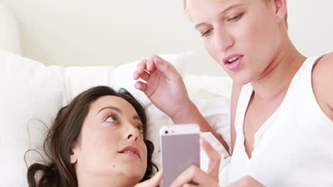 Lesbian-couple-lying-in-bed-using-phone