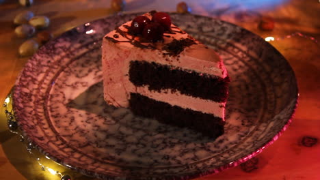 plate with a slice of dark chocolate cake topped with chocolate balls on table with lighting and scattered cashew nuts