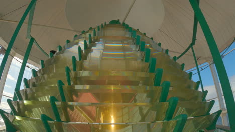 slow tilt shot, indoors looking up at the top of the fresnel lens of a lighthouse in motion with the lamp on during the day