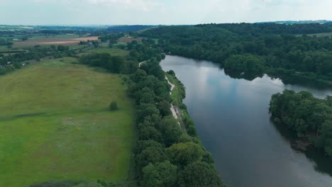 a tranquil nature filmed from above: a still lake, a vivid bright green forest, and a lawn on the left side of a lake