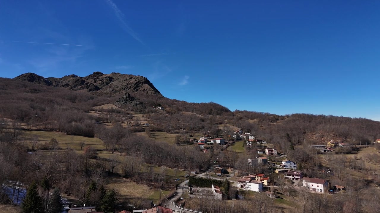 Pequeña aldea rural cerca de Monte Lama en los Apeninos septentrionales de Emilia-Romaña, Italia, rodeada de bosque montañoso, campos en terrazas y casas aisladas en la ladera, toma aérea de paisaje con dron.