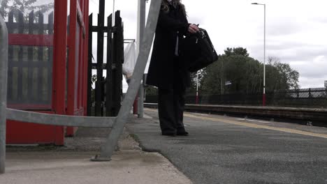 business woman waiting at train with briefcase wide shot