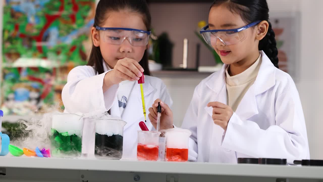 Two young students in lab coats and goggles perform a science experiment with colorful liquids