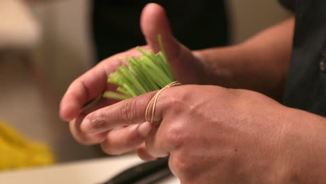 Tying-A-Bunch-Of-Green-Chives-With-A-Rubber-Band---Sushi-Preparation---close-up,-slow-motion