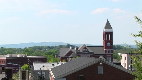 the camera pansright across the roofline of a small town to highlight an old clock tower