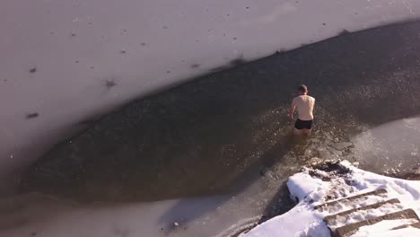 aerial view of young man entering frozen lake in winter through broken ice