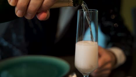 Pouring-bubbling-champagne-in-tuxedo-into-into-tall-glass-at-party