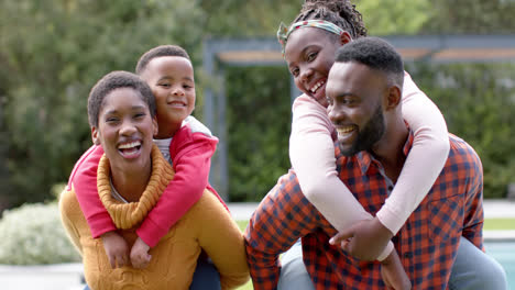 Retrato-De-Felices-Padres-Afroamericanos,-Hijo-E-Hija-Abrazándose-Y-Sonriendo-En-Un-Jardín-Soleado