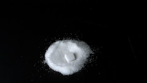 sugar cube falling into pile of sugar on black surface