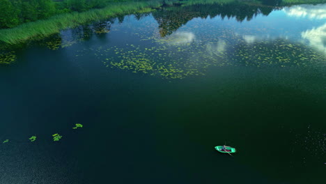 tiny-boat-in-big-lake,-empty-pond,-lonely-small-vessel,-green-big-outdoor-body-of-water,-sky-reflection-in-water-surface,-aerial-shot-with-sunny-weather,-drone-overview