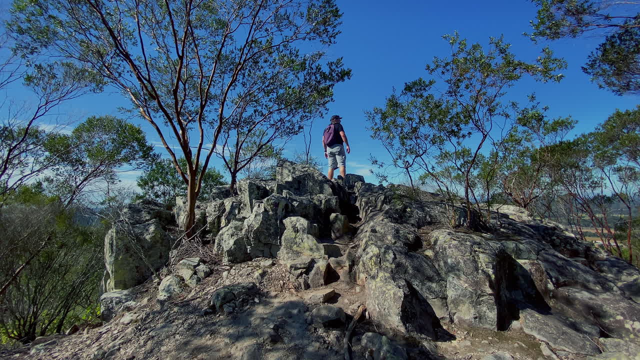 Middle aged man hiking up small rocks to summit of Mount Coochin, Glasshouse Mountains, Queensland