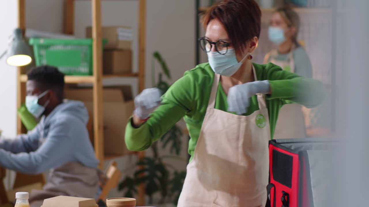 Donna con la mascherina che prepara pasti e bevande in una borsa per la consegna di cibo