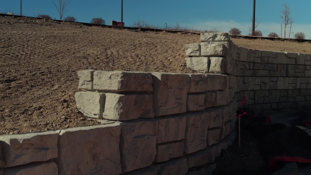 Handheld pan past stacked stone retaining wall and graded dirt slope in daylight