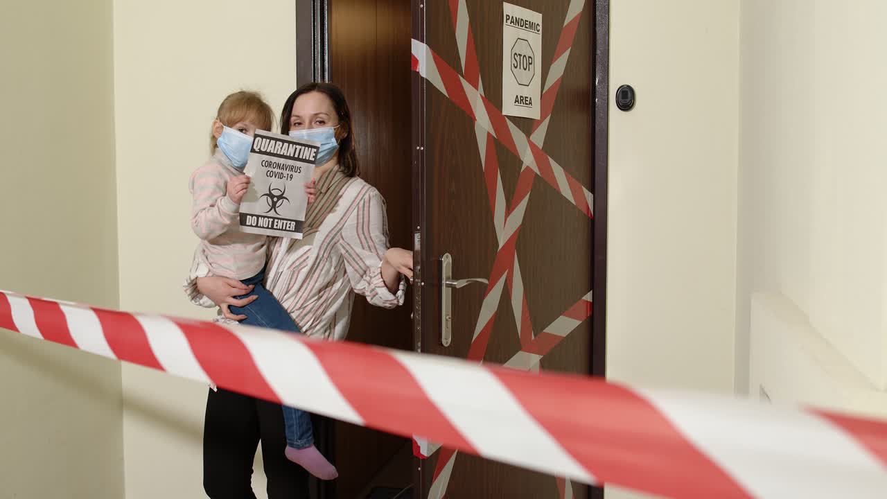 Madre malata con la figlia piccola, entrambe con mascherine mediche, che aprono la porta di casa, durante il lockdown per la quarantena da coronavirus.