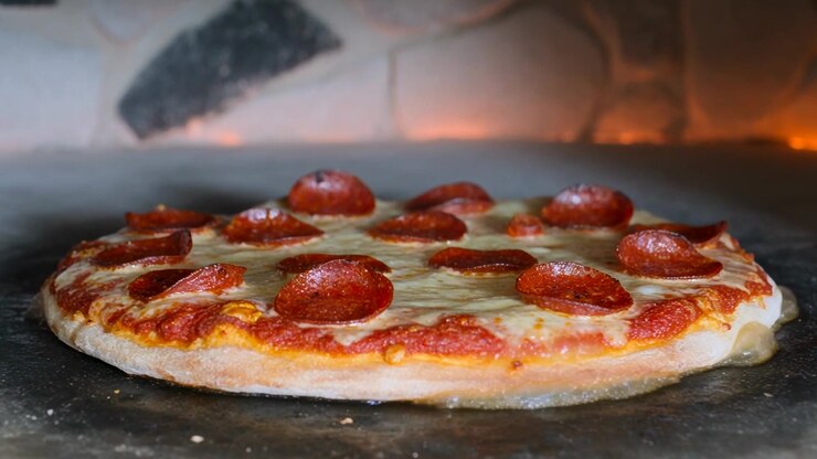Posizionare una pizza ai peperoni che cuoce sul fondo di un forno in pietra, con il formaggio che si scioglie e i peperoni che si arricciano, per cena.