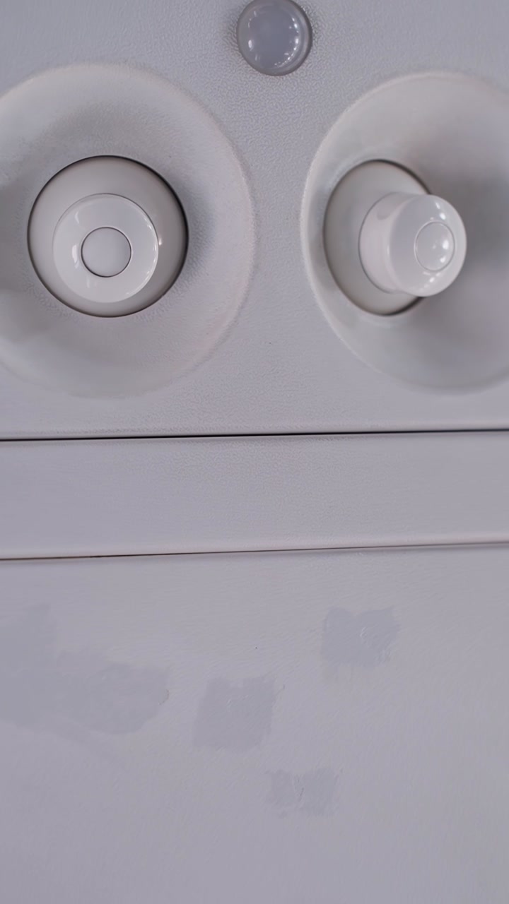 Vertical close-up of an airplane cabin panel with air vents and faint passenger service icons, showing minimal inflight interior details in soft neutral light.