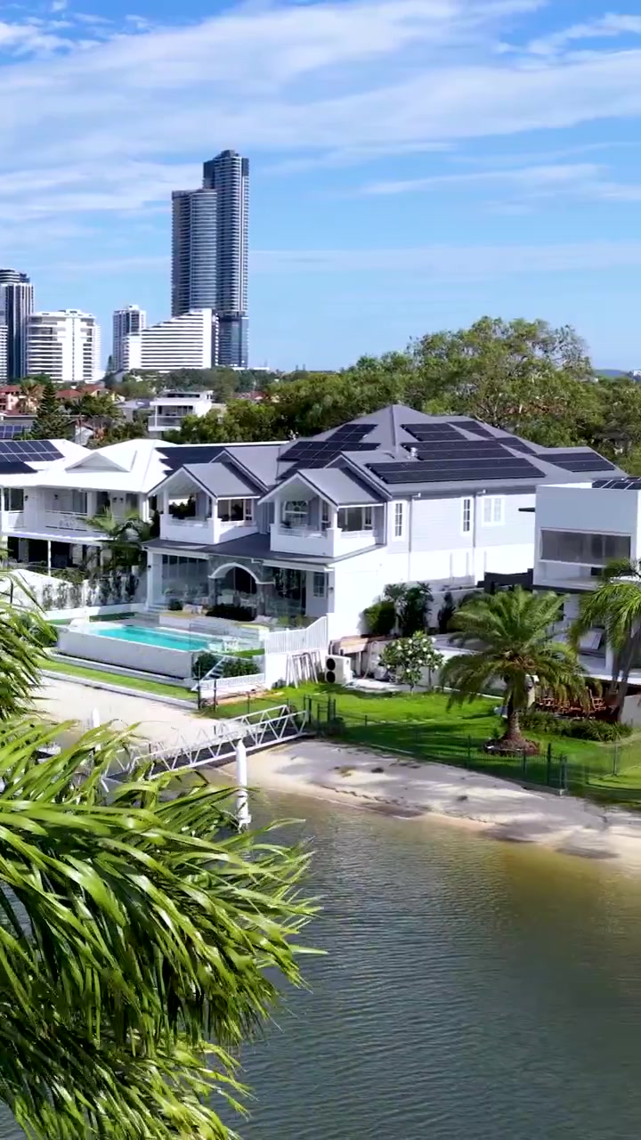 Un dron sobrevuela palmeras, revelando casas modernas junto al canal, barcos y el horizonte de la ciudad de Gold Coast.