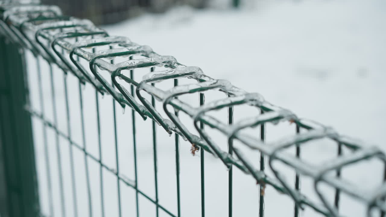 primer plano de una valla de cadena verde cubierta de caramelos de hielo, situada contra un paisaje nevado borroso, que representa el frío absoluto del invierno con un enfoque en texturas heladas