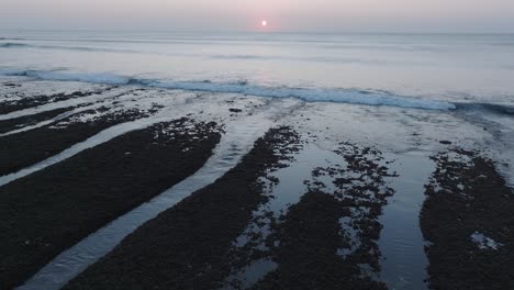 Low-Angle-Drone-shot-descending-on-Bingin-Beach-low-tide-reef-with-sunset-in-Uluwatu-Bali-Indonesia