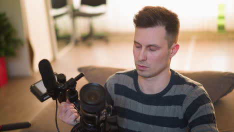 broadcast director preparing camera gear, focusing on lens adjustments with microphone, light setup, and camera on table in home studio setting, getting ready for filming or production
