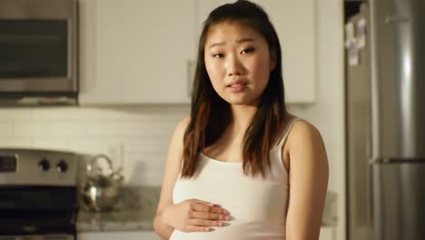 a reflective journey: a young woman in her kitchen, embracing the anticipation of motherhood, with a calm and thoughtful expression as she touches her baby bump