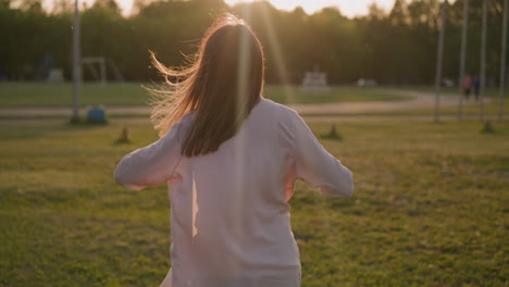 Woman-in-loose-pink-shirt-walks-along-lawn-in-city-park