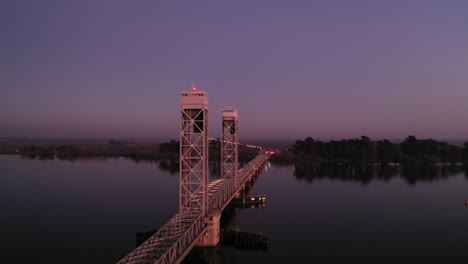 drone passes over vertical lift bridge crossing sacramento river in california at dusk