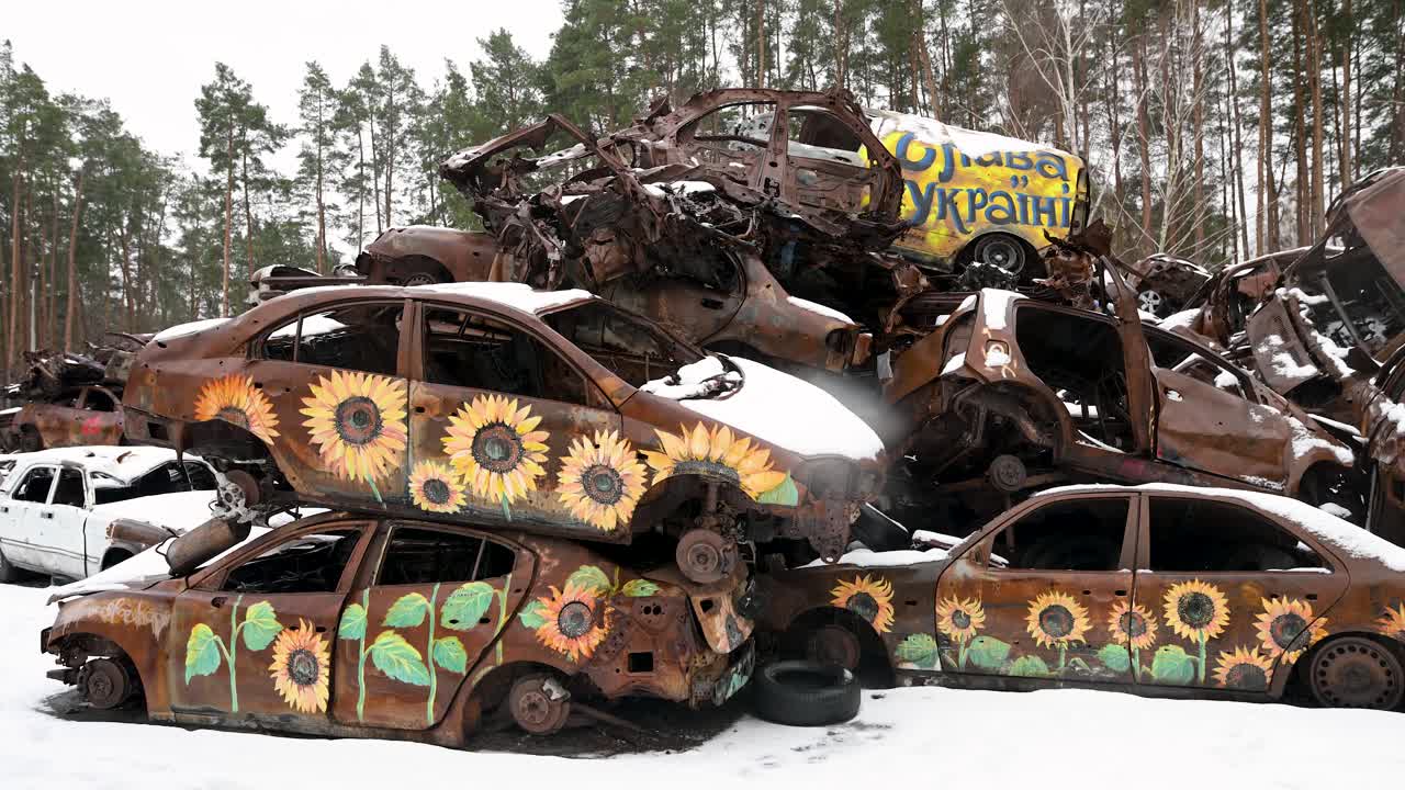 In Irpin, Ukraine, a winter scene shows a pile of burnt and wrecked cars, some adorned with sunflower paintings, following intense battles between Ukrainian and Russian forces.