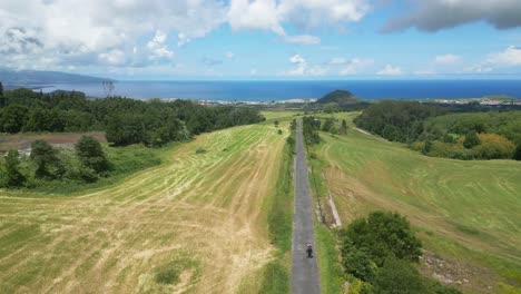 un camino pintoresco se extiende a través de campos verdes con una vista lejana de la lagoa do fogo y el mar